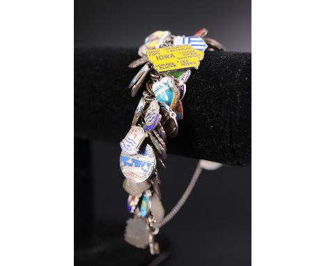 A vintage silver / white metal charm bracelet containing a large number of regional enamelled and other shield charms etc, 10
