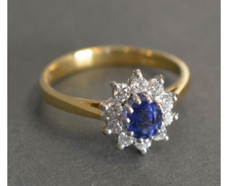 An 18ct. Yellow Gold Sapphire and Diamond Cluster Ring, with a central oval sapphire surrounded by diamonds within a pierced 