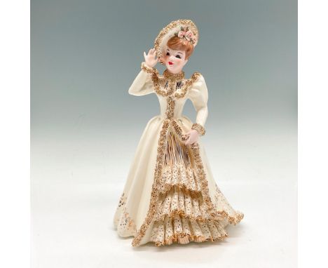 Glossy figural dressed in white and gold tones with overcoat embellished with gilt down the edges and ruffled dress with simi