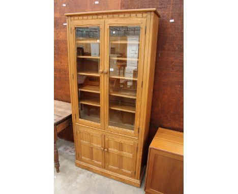 A BLONDE ERCOL ELM TWO DOOR GLAZED CABINET WITH CUPBOARDS TO BASE, 37" WIDE 