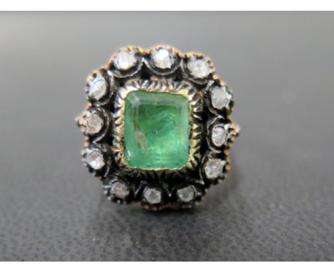 An emerald and diamond cluster ring - The octagonal emerald within a rose-cut diamond surround - Tests as higher carat gold a