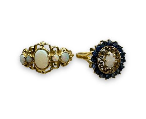 Two 9ct gold opal set dress rings. Comprising a 9ct gold scrollwork ring set with five opals en cabochon, with carved shoulde