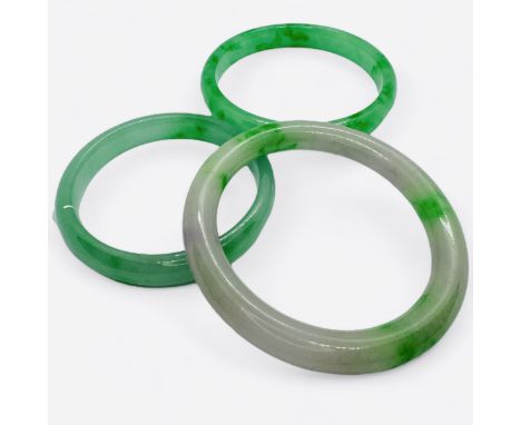 Three jadeite bangles, of graduating sizes.  The first, a "floating flower" green and white jade bangle has an internal diame