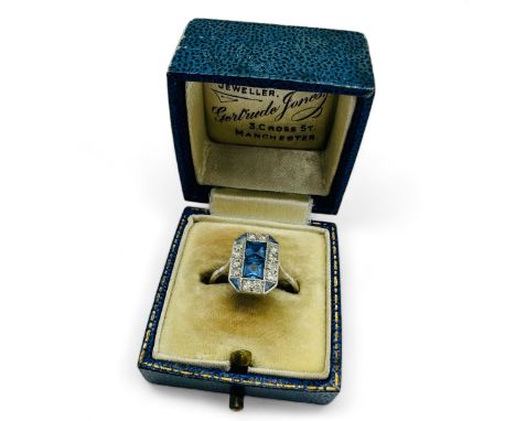 An Art Deco sapphire and diamond set panel ring. Set with two central square cut pale blue sapphires, framed by twelve old ei