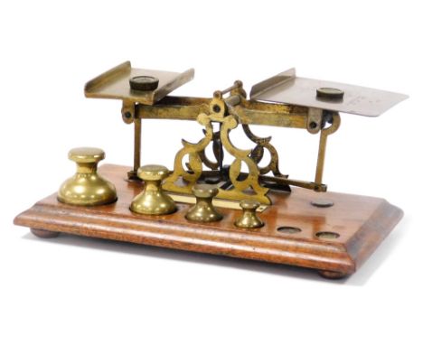 A set of early 20thC brass postal scales, with weights, on a wooden base, 24cm wide.