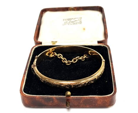 A 9 ct gold hinged bangle, 6 cm, 10.7 g, in box with 18 ct gold chain which is sewed into the box lining.&nbsp;
