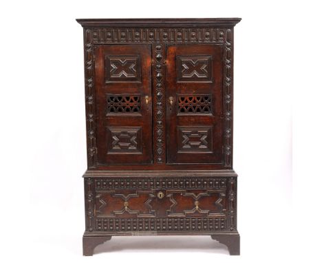 AN ANTIQUE OAK CABINET with shaped and moulded decoration and geometric panelled doors, above a fitted drawer and standing on