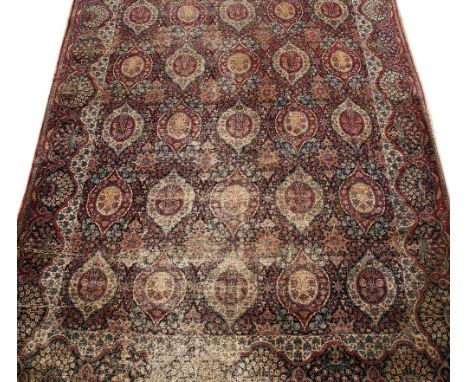 A PERSIAN RED AND BLUE GROUND CARPET with five rows of six foliate motifs and all over foliate geometric decoration, 404cm x 