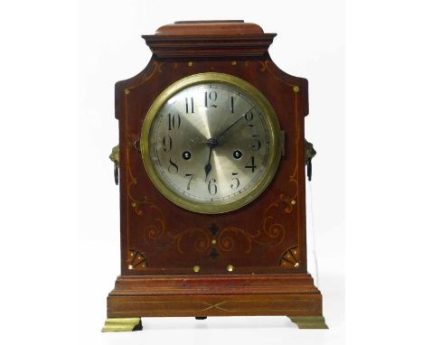 A 20th century mahogany bracket clock with caddy top and inlaid marquetry design. Silvered dial with Arabic numerals. Two tra