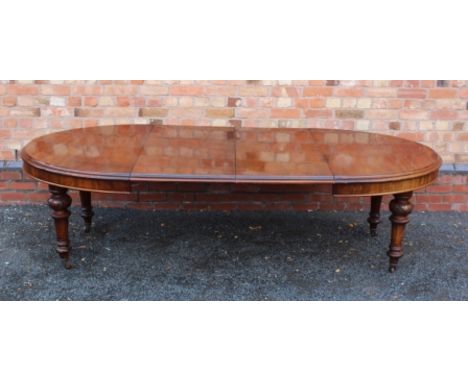 A 19TH CENTURY MAHOGANY FINISHED OVAL EXTENDING DINING TABLE on four turned and carved tapering legs, with brown ceramic cast