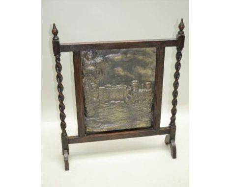 AN EDWARDIAN OAK FRAMED FIRE SCREEN inset embossed brass panel "Warwickshire Castle", to top of frame finials, 74.5cm 