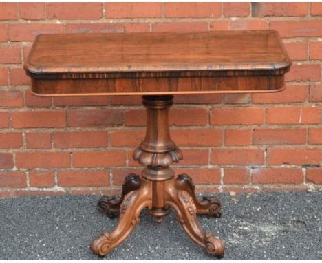 A 19TH CENTURY ROSEWOOD FOLDOVER CARD TABLE, baize lined supported on a carved turned baluster column and four carved scrolli