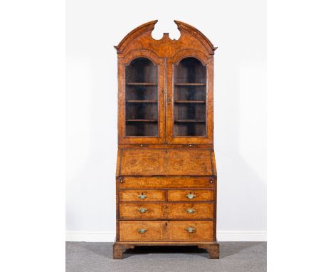 A George II walnut bureau bookcase, with herringbone stringing and cross banding, broken elliptical pediment, two arched glaz