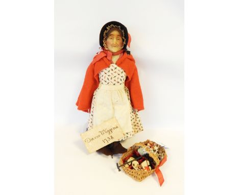 Late 19th century wax head doll of old lady, soft body, wax hands, wearing printed dress and red cape and bonnet, carrying ba