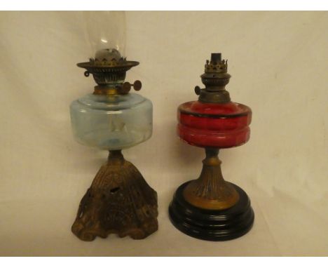 A Victorian brass oil lamp with cranberry-tinted glass reservoir (af) and one other cast iron and brass oil lamp with aqua gl