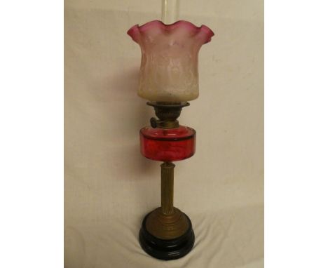 A Victorian brass oil lamp with column stem, cranberry-tinted glass reservoir and etched cranberry-tinted glass floral shade 