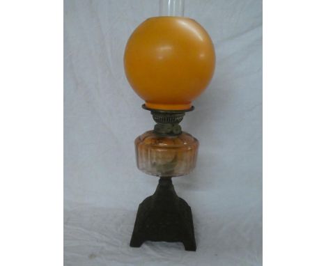 A Victorian cast iron and brass mounted oil lamp with orange-tinted glass reservoir and orange opaque glass shade