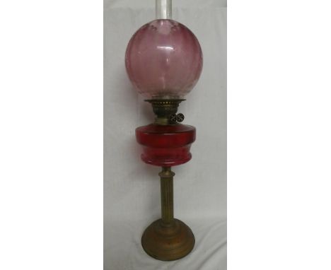 A Victorian brass oil lamp with column stem, circular cranberry-tinted glass reservoir (hairline crack) and cranberry tinted 