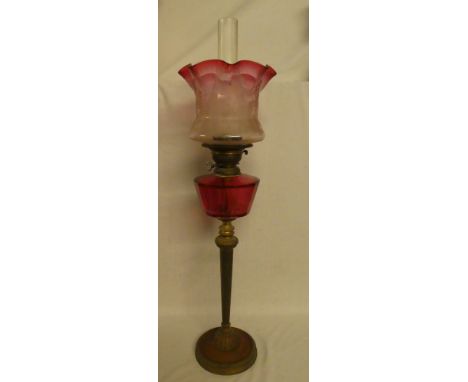 An Edwardian tall brass and copper oil lamp with cranberry-tinted glass reservoir and cranberry-tinted floral shade (shade wi