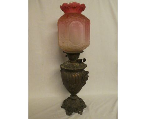 A Victorian coppered spelter pedestal oil lamp with raised scroll decoration and detachable font surmounted by a cranberry-ti