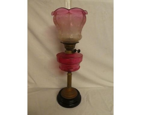 A Victorian brass oil lamp with fluted stem, cranberry-tinted glass reservoir and cranberry-tinted floral etched glass shade 