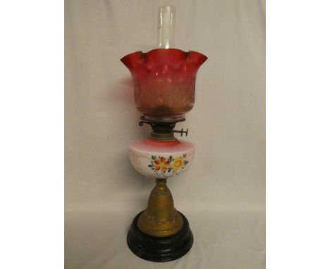 A Victorian brass oil lamp with opaque glass floral reservoir and cranberry-tinted floral shade on ceramic base (shade with t