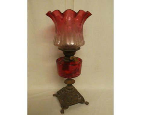 A Victorian cast iron and brass oil lamp with cranberry-tinted glass reservoir and cranberry-tinted foliate shade (shade dama