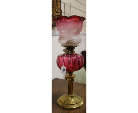 A cranberry glass oil lamp with cranberry shade and two others, smaller with shades