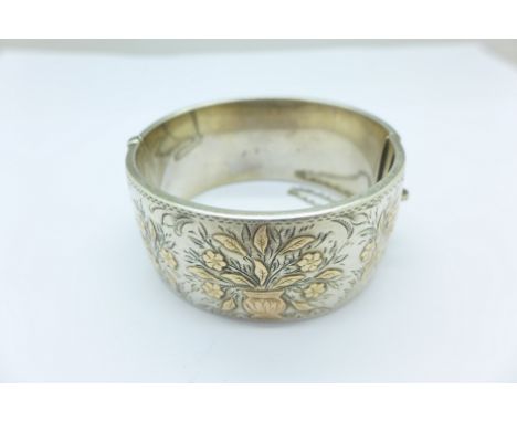 A hallmarked silver bangle with gold applied decoration