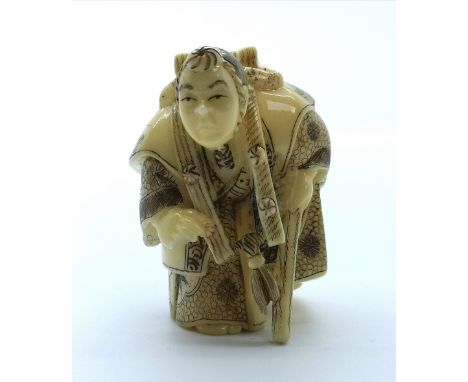A signed carved ivory Japanese netsuke of a travelling man with a box on his back