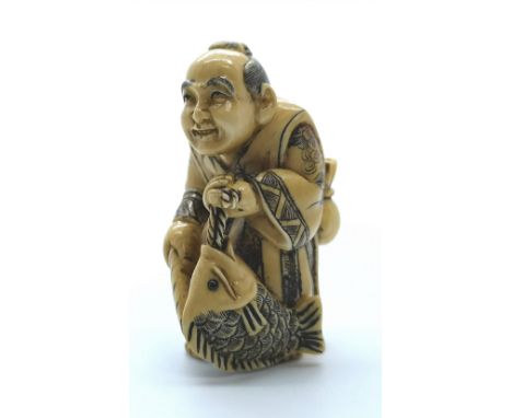A signed carved ivory Japanese netsuke of a man catching a fish