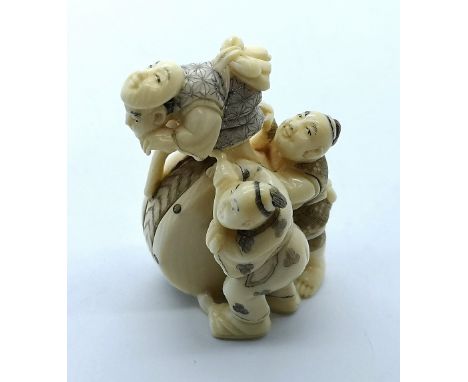 A signed carved ivory Japanese netsuke of a Noh actor balanced on a large drum supported by two men