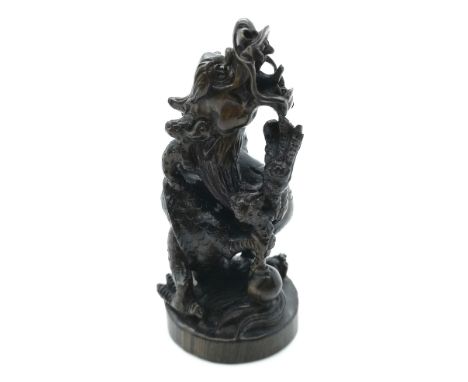 A signed carved wooden Japanese netsuke of a dragon with its foot on a ball representing the world