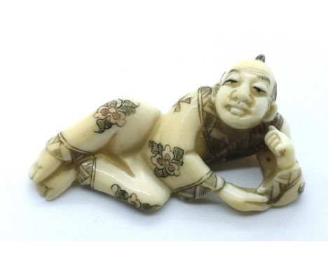 A signed carved ivory Japanese netsuke of a recumbent man 