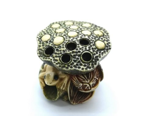 A signed carved ivory Japanese netsuke of a frog seated on a lily pad under a lotus pod