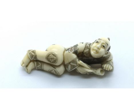 A signed carved ivory Japanese netsuke of a reclining man with an opium pipe