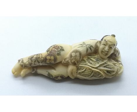 A signed carved ivory Japanese netsuke of a man lying down holding a large Hakusai preparing for winter