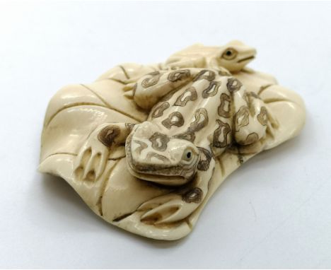 A signed carved ivory Japanese netsuke study of a frog and a toad on a lily pad