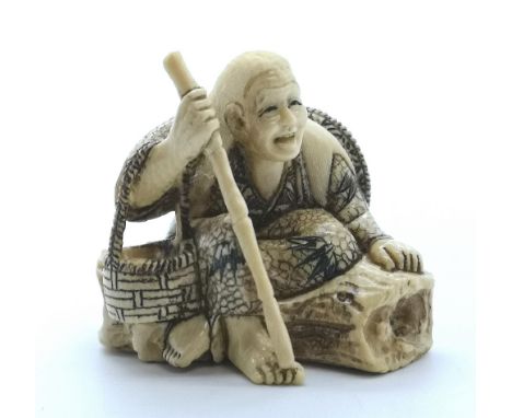 A signed carved ivory Japanese netsuke of on old man resting on a log with a basket and a stick