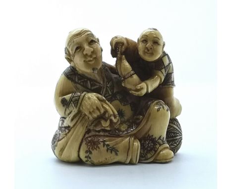A signed and carved ivory Japanese netsuke of a seated man and young boy
