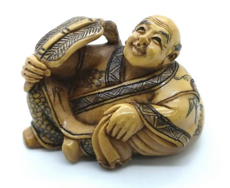 A signed carved ivory Japanese netsuke of a village elder relaxing in the heat