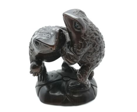 A carved signed fruitwood Japanese netsuke of two toads fighting on a lily pad for the world depicted as a ball