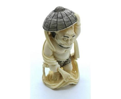 A carved and signed ivory Japanese netsuke of a demon disguising his head with a basket