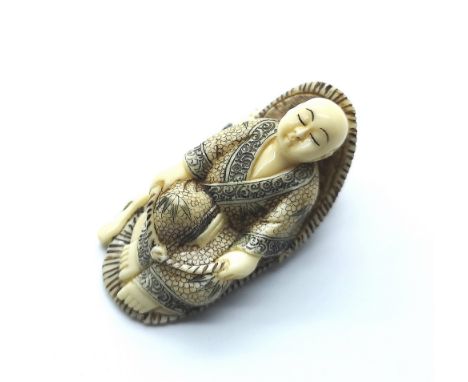 A signed carved ivory Japanese netsuke a study of a man lying in a chair