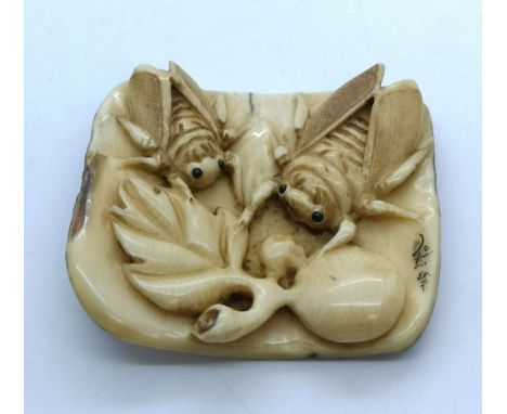 A carved and signed Japanese netsuke of two insects feeding while resting on a piece of bark