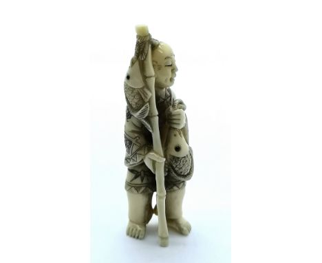 A signed carved ivory Japanese netsuke of a fisherman with his catch displayed in his left hand and a bamboo staff held in th