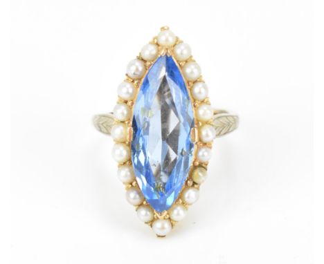 A yellow metal, seed pearl and blue stone navette ring, with central blue cut stone in a halo of seed pearls, flanked with le