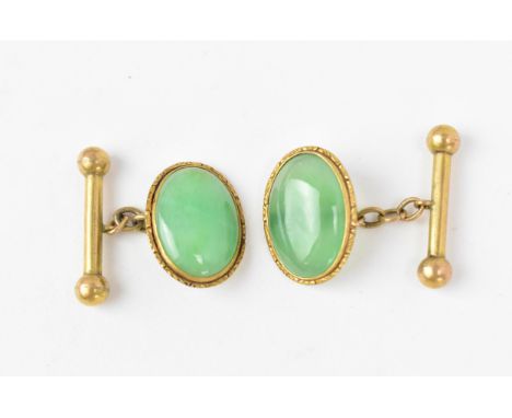 A pair of yellow metal and jade cuff links, with central oval cabochon green jade in a yellow metal frame with pattern border