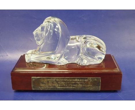 A Steuben art glass model of a recumbent lion designed by Lloyd Atkins, with wooden plinth base, the plinth with later applie