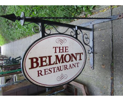 An exterior iron work wall mounted sign bracket with scroll work detail and oval frame housing a painted metal restaurant sig